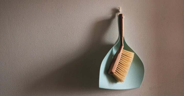 light blue dustpan and natural dust brush hang from a beige wall