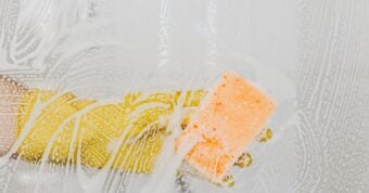 Hand with yellow glove holding sponge cleaning glass surface.