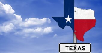 The state of texas on a sign with the texas flag surrounded by clouded skies.