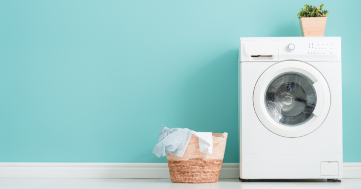 Photo of a laundry basket beside a washing machine with a plant on top against a light blue background