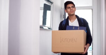 A man wearing a book bag holding a box labeled "kitchen"