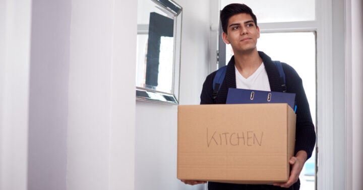 A man wearing a book bag holding a box labeled "kitchen"